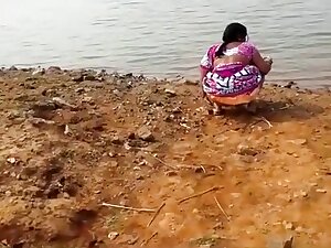 Indian woman peeing in the dirt by a lake